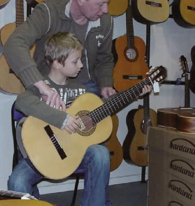 Een kind krijgt in de winkel een klassieke gitaar aangemeten.